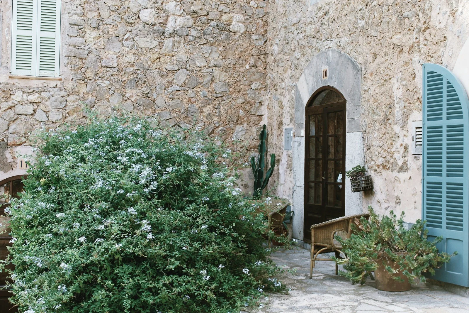 Altes Steinhaus mit blauen Fensterläden und blühendem Strauch in Deià auf Mallorca